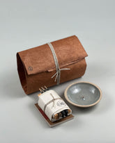 A product shot showing the Incausa Home Bundle brown paper wrapped parcels along with its contents of incense and incense holder. Set on a seamless, light grey background.