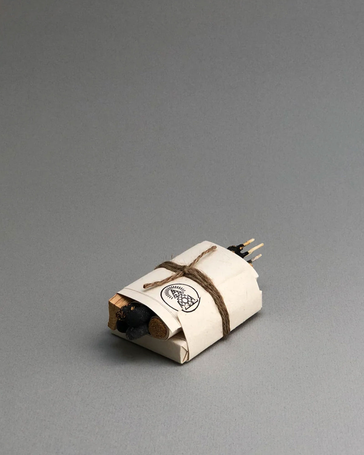 A bundle of incense wrapped in white paper and string on a seamless, grey background. 