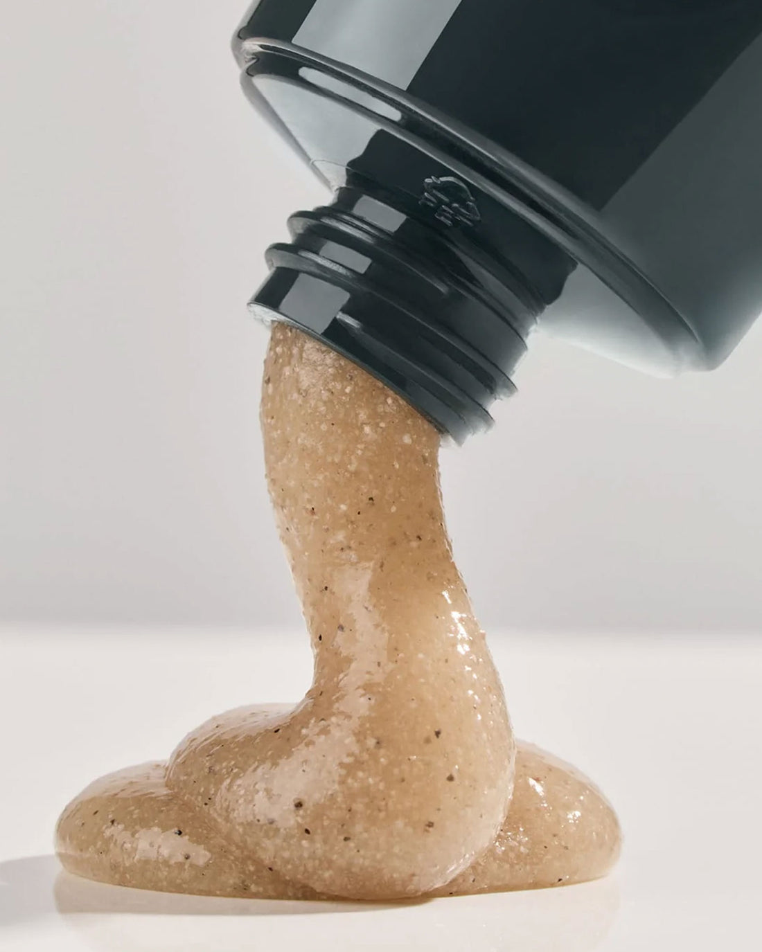 A squeeze tube of Leif Caviar Lime Body Scrub, a navy blue bottle with a light brown, semi-translucent, textured cream coming out of the nozzle. 