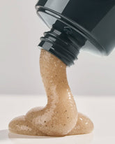 A squeeze tube of Leif Caviar Lime Body Scrub, a navy blue bottle with a light brown, semi-translucent, textured cream coming out of the nozzle. 