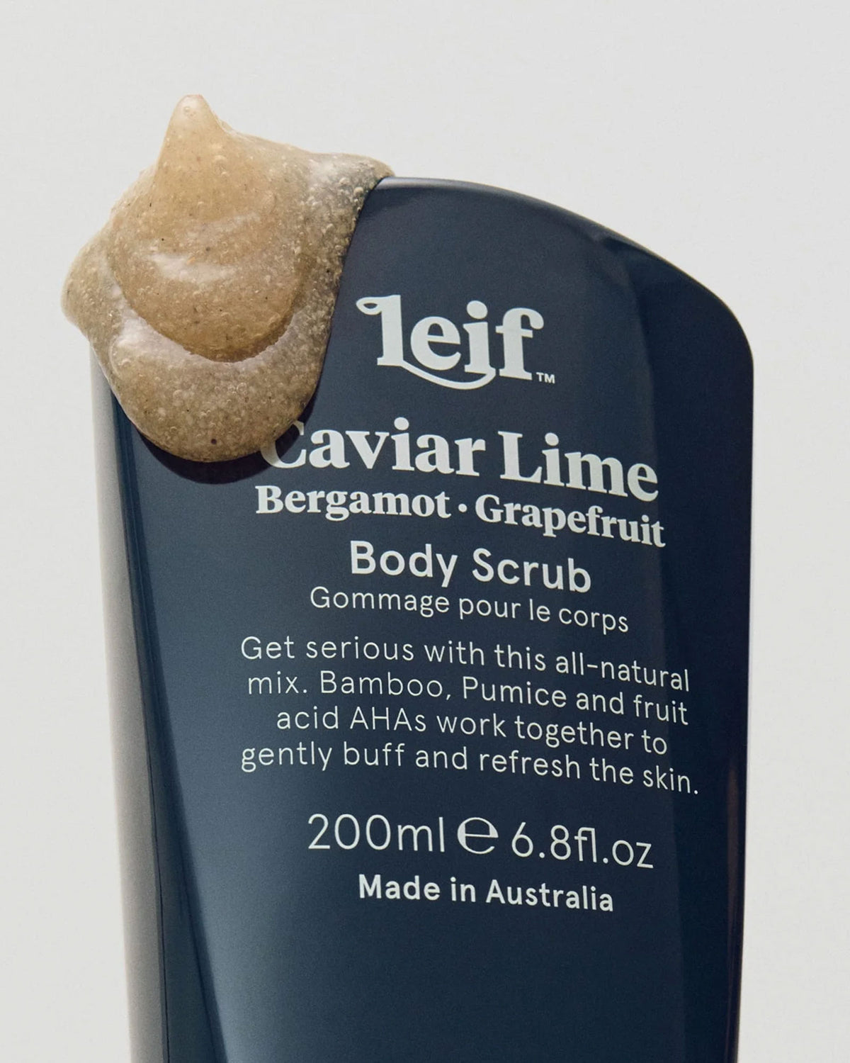 Leif Caviar Lime Body Scrub in a dark navy blue squeeze bottle, with a dollop of the beige scrub visible at the top against a light grey background.