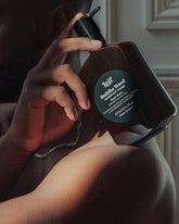 A man holding a 500ml dark amber bottle of Leif Buddha Wood hand Cleanser on his shoulder.