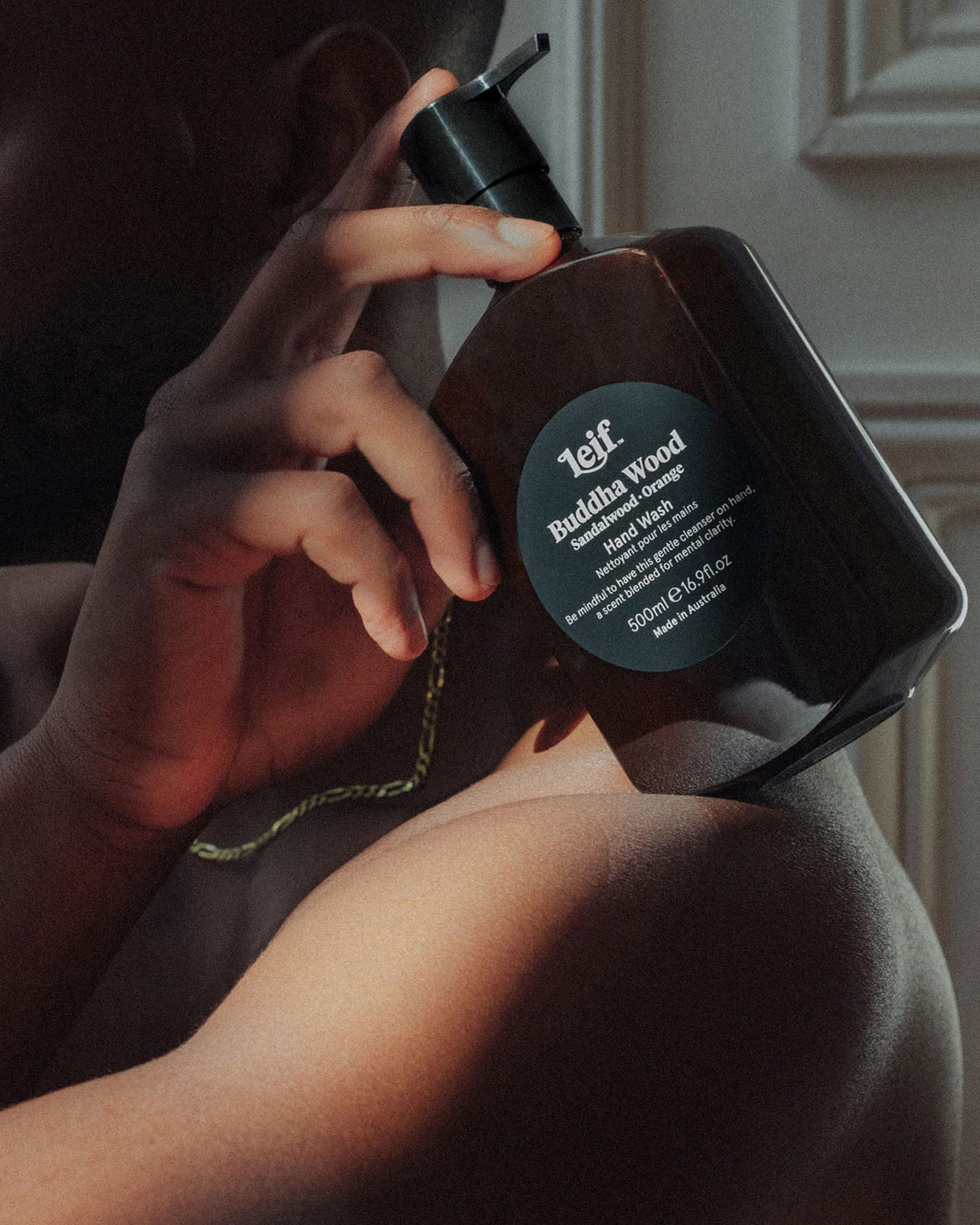 A man holding a 500ml dark amber bottle of Leif Buddha Wood hand Cleanser on his shoulder.