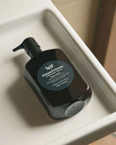 A 500ml dark amber bottle of Leif Flannel Flower Hand Cleanser laying flat inside a recessed surface.