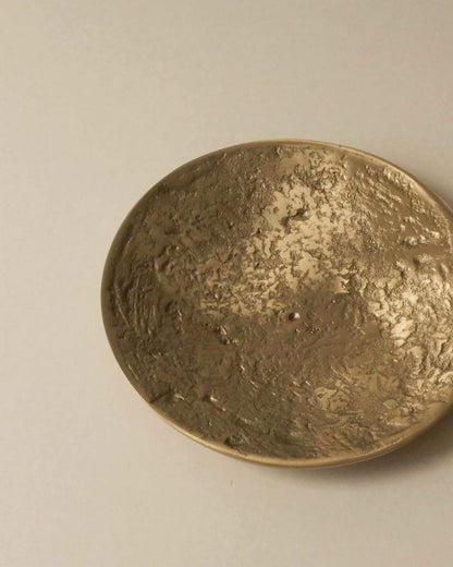 A round brass textured plate on an off-white table surface.