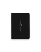 A black hardcover notebook featuring the Cancer zodiac sign and its chart symbols printed in metallic on the front cover, set against a clean white background.