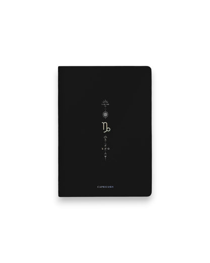 A black hardcover notebook featuring the Capricorn zodiac sign and its chart symbols printed in metallic on the front cover, set against a clean white background.
