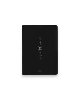 A black hardcover notebook featuring the Gemini zodiac sign and its chart symbols printed in metallic on the front cover, set against a clean white background.