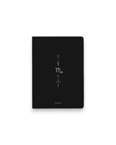 A black hardcover notebook featuring the Scorpio zodiac sign and its chart symbols printed in metallic on the front cover, set against a clean white background.