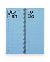 An open spread of a tall, rectangular ring-bound day planner with blue pages set on a solid white background. 