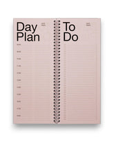 An open spread of a tall, rectangular ring-bound planner with light pink pages, set on a solid white background. 