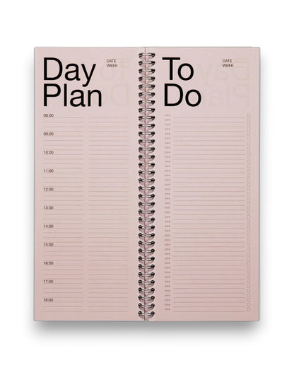 An open spread of a tall, rectangular ring-bound planner with light pink pages, set on a solid white background. 