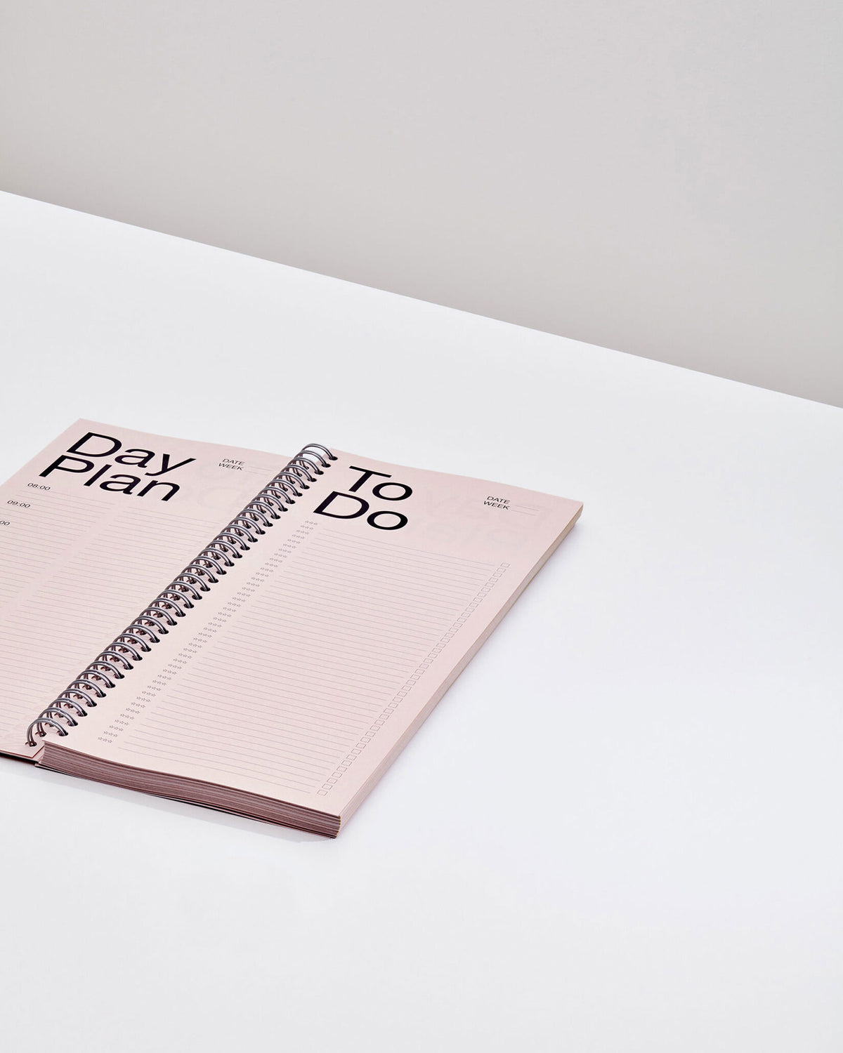 An open tall, rectangular ring-bound planner with light pink pages on a white table surface.