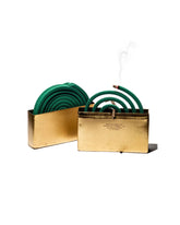 Two brass metal box halves on a white background, one containing several green mosquito coils and the other showing a burning green mosquito coil suspended in the brass box by a brown stick. Set on a white background.
