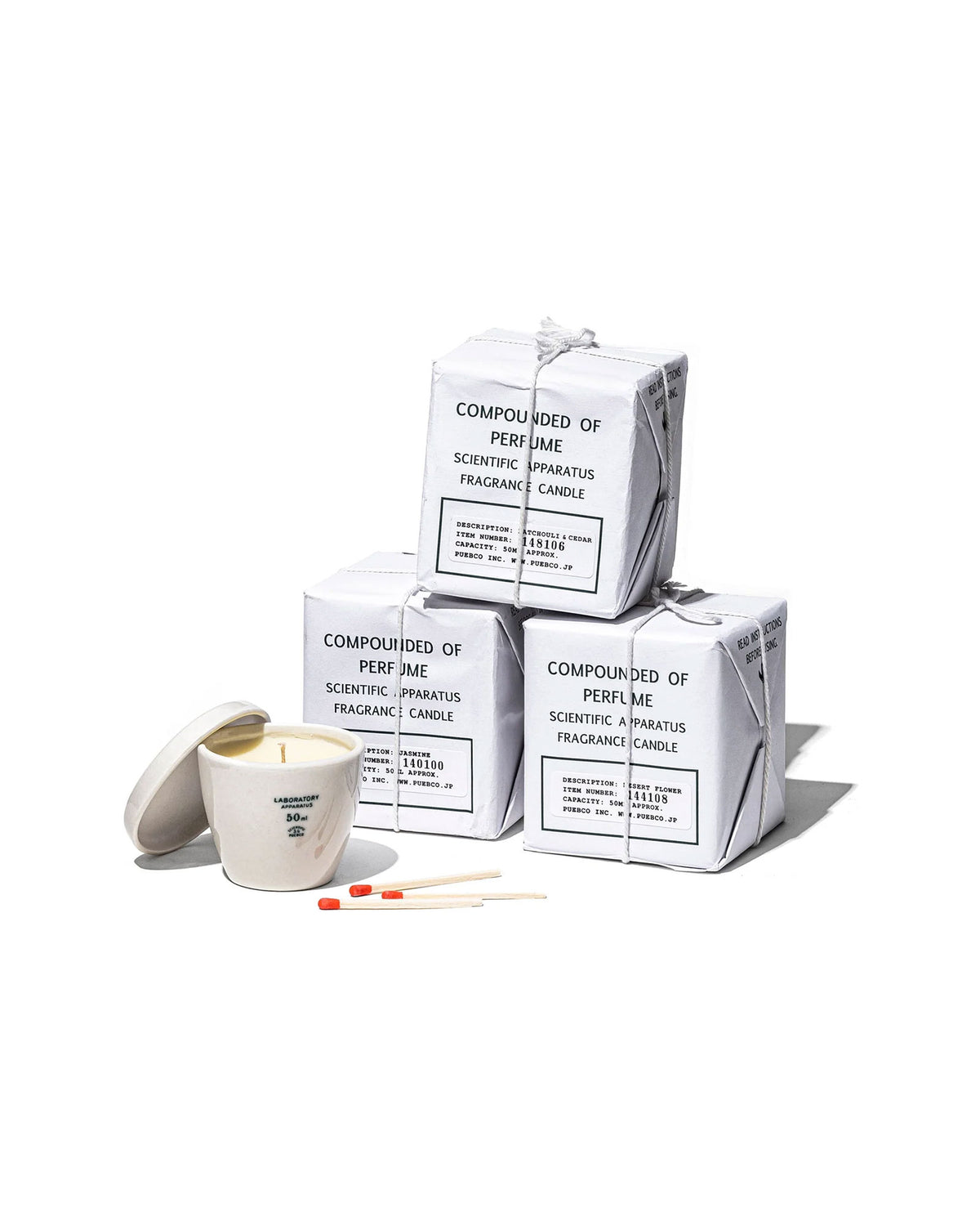 A stack of three Puebco Scientific Candles boxed next to one candle unboxed, set on a white background. 