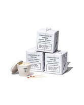 A stack of three Puebco Scientific Candles boxed next to one candle unboxed, set on a white background. 