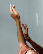 A woman applying a white cream to her arm against a light blue backdrop.