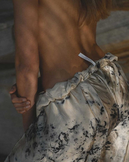 Close-up back view of a person wearing a cream-colored, tie-dye style pants with mottled patterns and a gathered elastic waist.