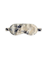 A silk eye mask with a marbled pattern in cream, beige, and dark navy blue, shown against a plain white background.