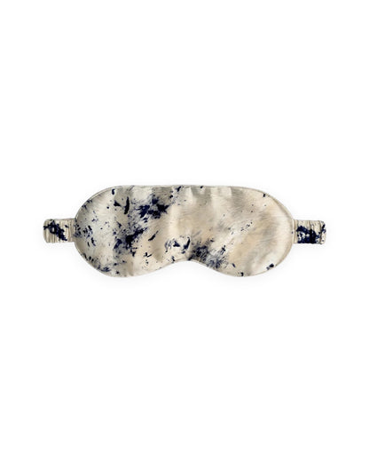 A silk eye mask with a marbled pattern in cream, beige, and dark navy blue, shown against a plain white background.