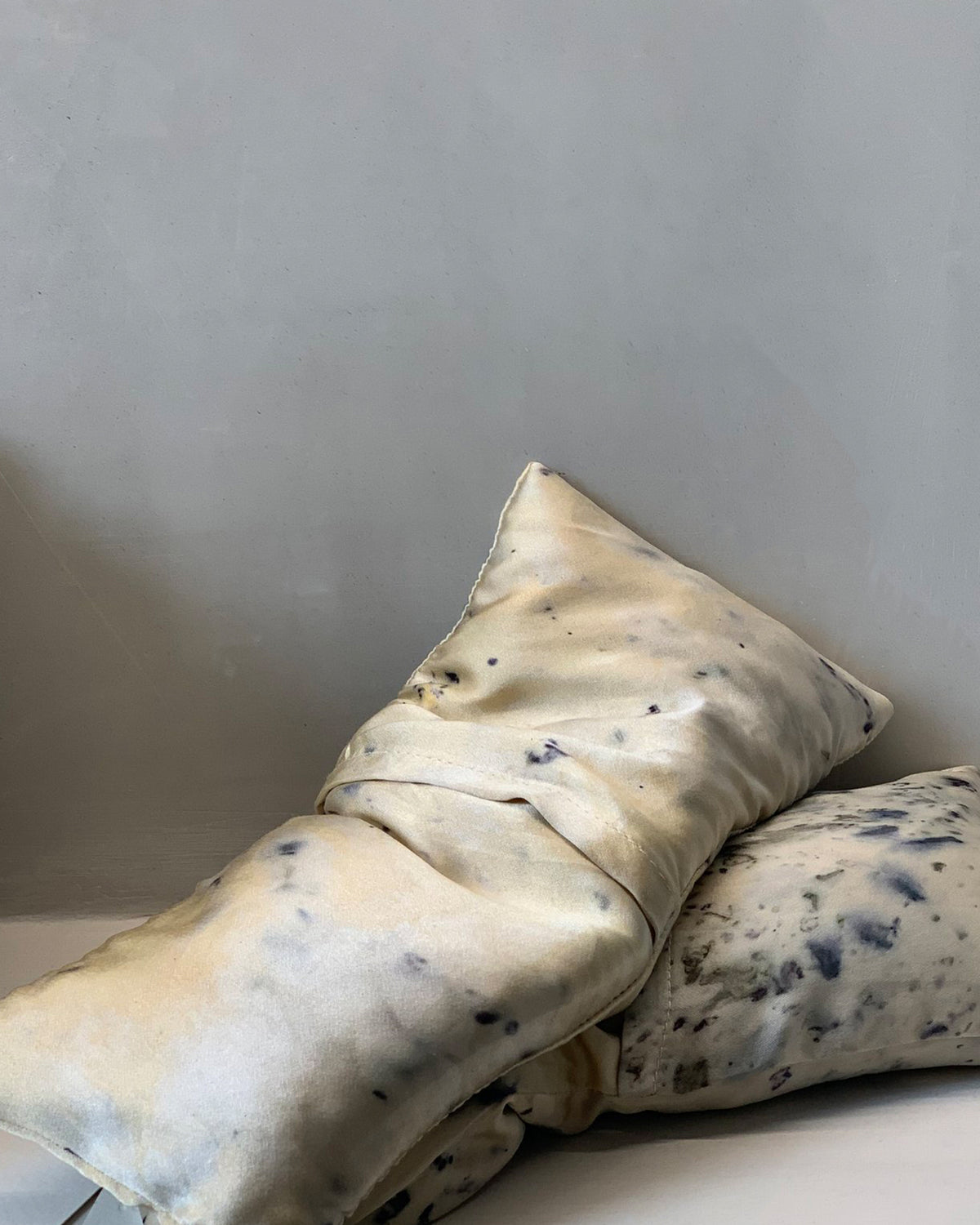 Two weighted eye pillows with mottled blue and beige abstract patterned silk slips.
