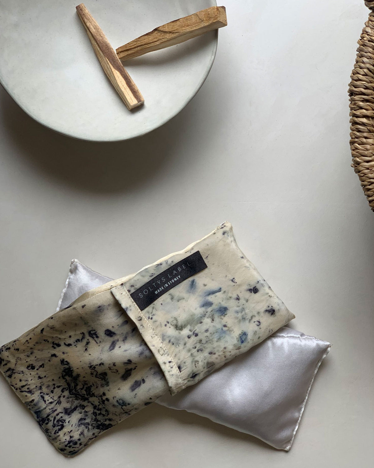 On a concrete surface next to a ceramic bowl with two sticks of Palo Santo wood, a Solty&