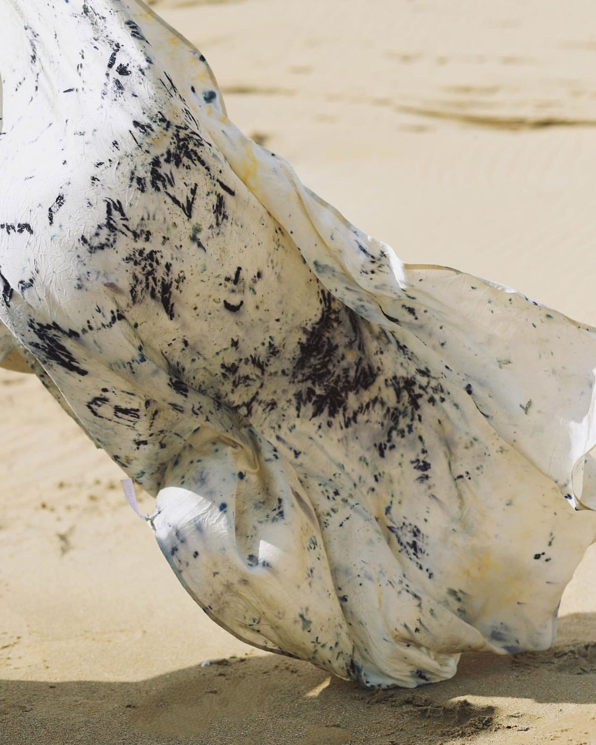 A piece of white and purple abstract coloured silk cloth blowing in the wind on a sandy backdrop.