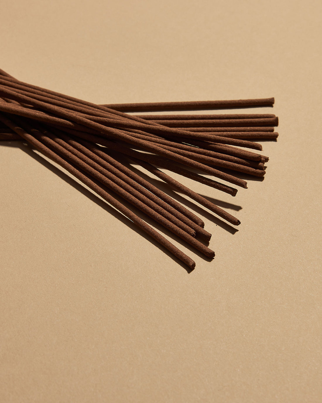A scattered pile of brown incense sticks on a soft orange background. 
