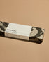 A closed grey marbled box of Subtle Bodies Peruvian Palo Santo Incense with a white wrap around label. Set on a light orange background. 