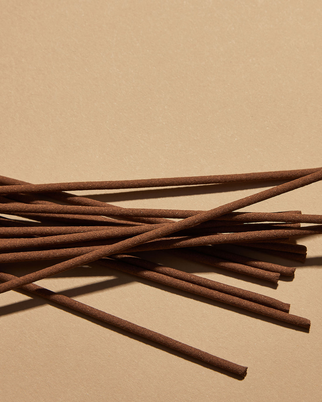 A scattered pile of brown incense sticks on a soft orange background. 