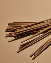 A scattered pile of brown incense sticks on a soft orange background. 