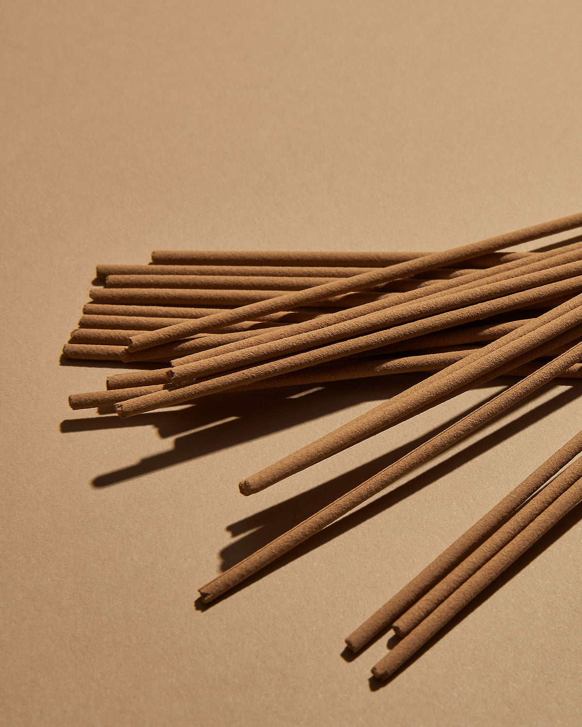 A scattered pile of brown incense sticks on a soft orange background. 