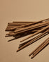 A scattered pile of brown incense sticks on a soft orange background. 