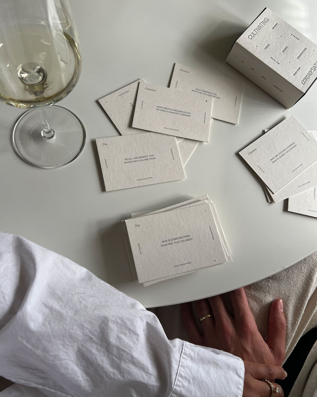 Birdseye view of half a round dining table with a wine glass with white wine and a box of Wilde House Paper&