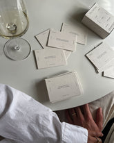 Birdseye view of half a round dining table with a wine glass with white wine and a box of Wilde House Paper&