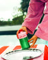 A person in a pink robe holds a green and pink bottle of Ya Albi&